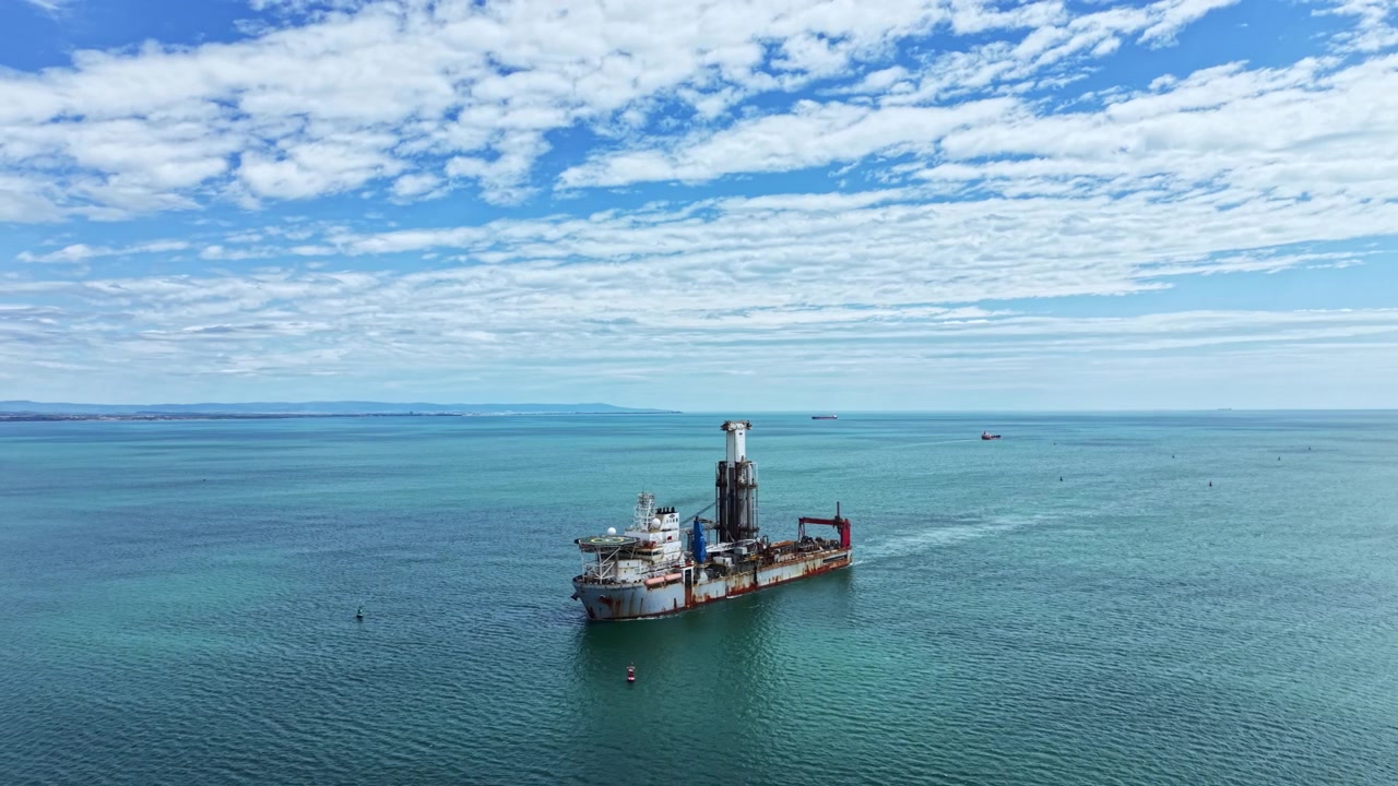 Industrial dredging vessel operates in open water under a clear sky with few clouds, focusing on dredging activities