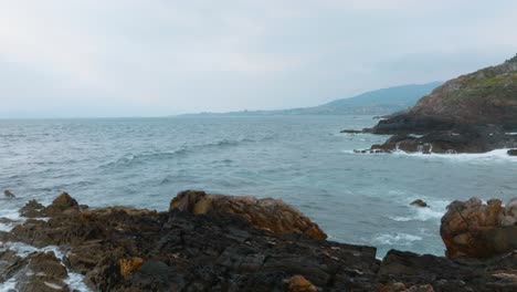 Drone-Volando-Bajo-Sobre-La-Playa-Rocosa-En-La-Costa-Azul-Del-Océano,-Mirador-De-Monteferro,-Vigo,-Galicia,-España