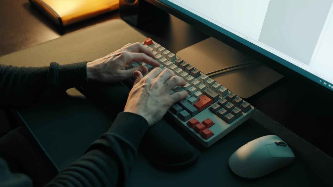 Mand sidder ved en computer og taster på et tastatur. Optagelse fra høj vinkel. Hjemmekontor.