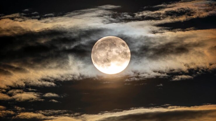 Faixas de nuvens em movimento, impulsionadas pela brisa, revelando e velando a lua cheia no céu noturno, com um halo luminoso.