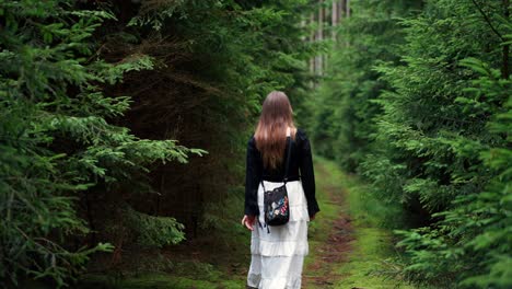 girl with long hair walks along a path in a coniferous forest during the day