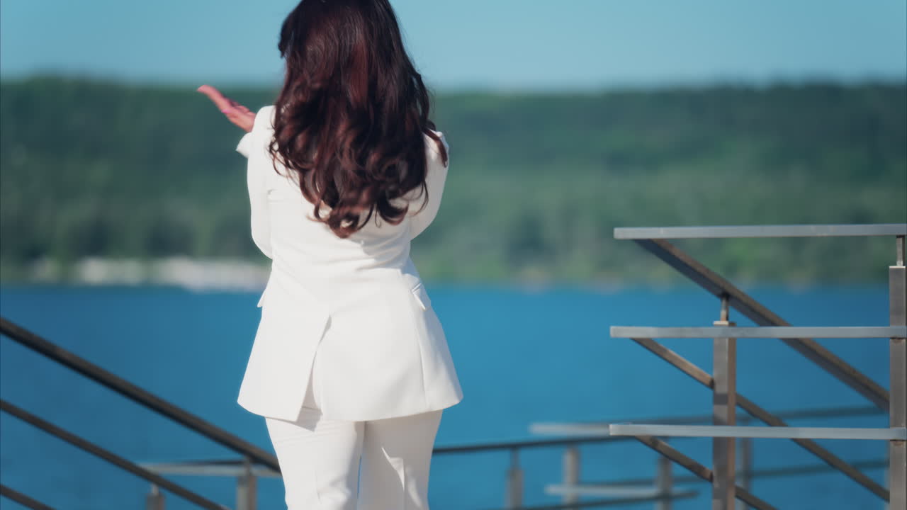 Woman in a white suit walking on a scenic terrace with a view of a calm body of water