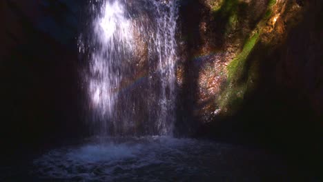 rainbow reflecting through waterfall flowing over moss covered rocks