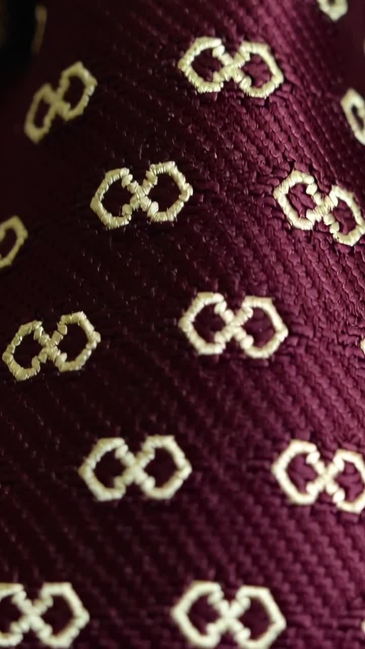 Vertical video: Shifting camera revealing maroon tie in macro, centering cream linked-loop motifs