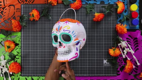 hands holding colorful day of the dead skull decoration on vibrant background, top view