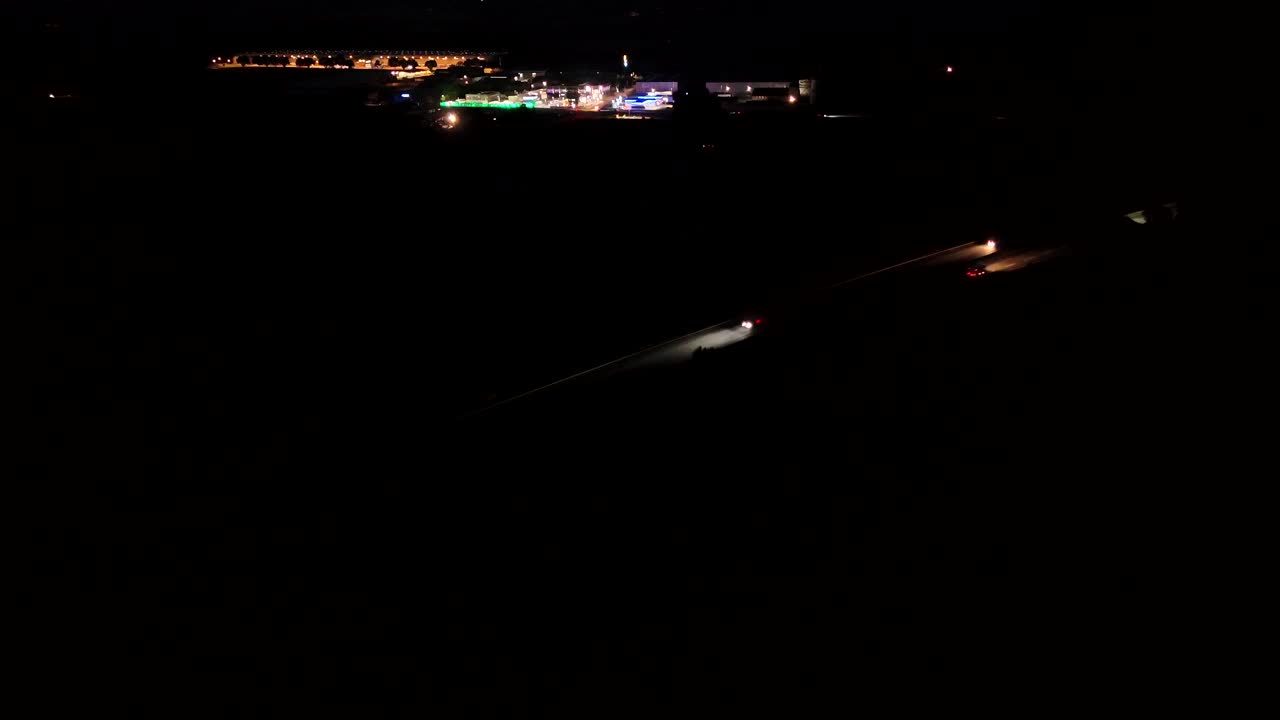Traffic on American highway with gas station and warehouses in industrial district. Night scene in summer. Aerial wide shot. Headlights and backlights on asphalt