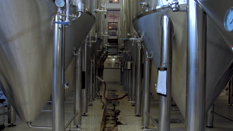 slow tilt up from floor drain to rows of large stainless steel beer fermentation tanks in a brewery