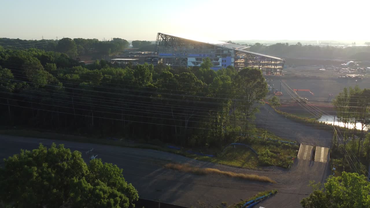 Descending shot of new Carolina Panthers practice facility after construction halted. Sun rises in the background and reflects from unfinished roof.