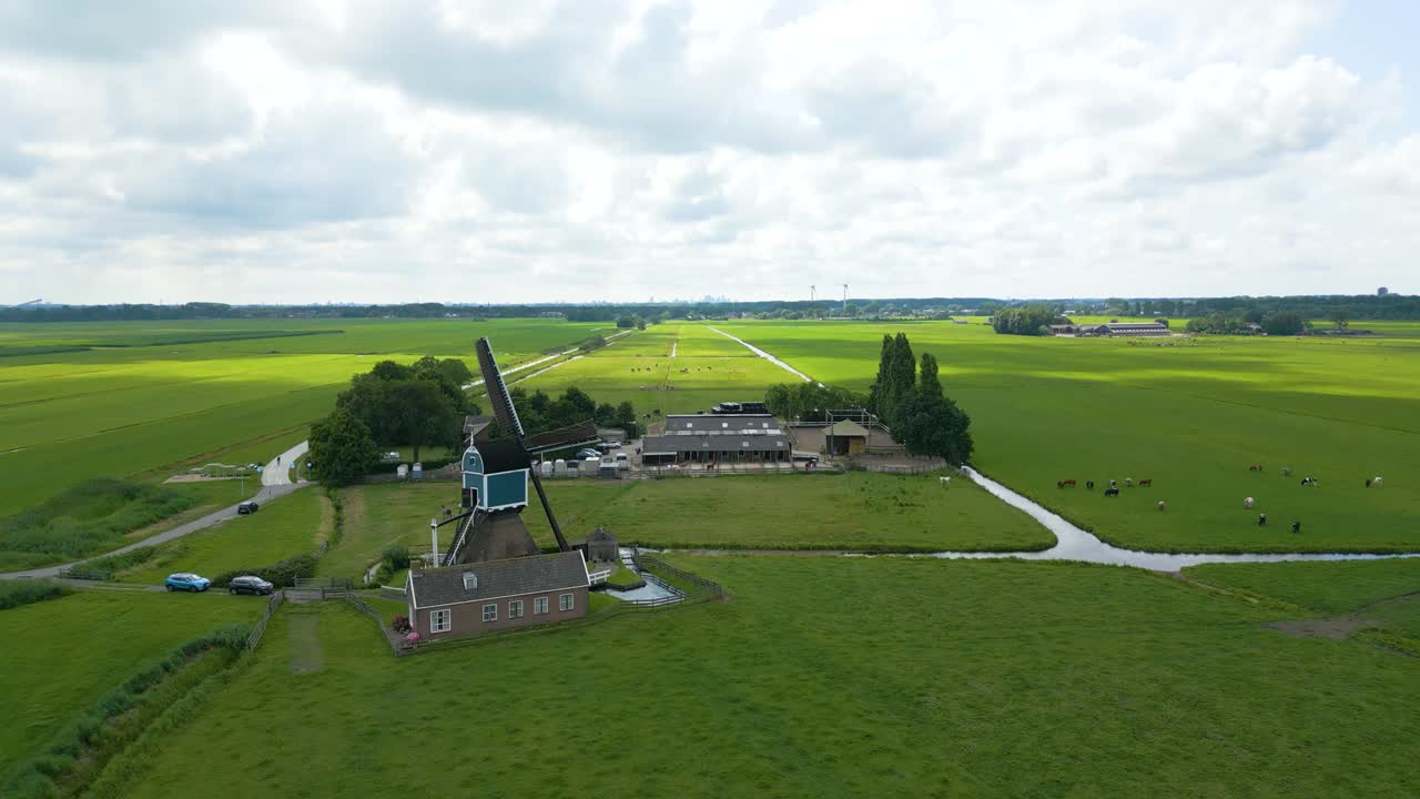 Wide drone view of a historic windmill sitting in a vast, open Dutch polder landscape. Peaceful and flat surroundings under a slightly cloudy sky