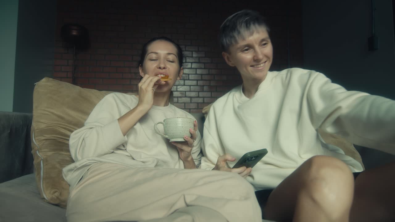 Two women relaxing together on the couch, enjoying coffee and snacks