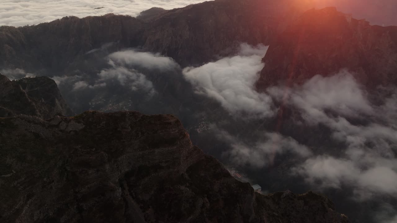 Golden sunset light illuminates thick clouds drifting through a steep valley beneath Pico do Arieiro in Madeira, Portugal.