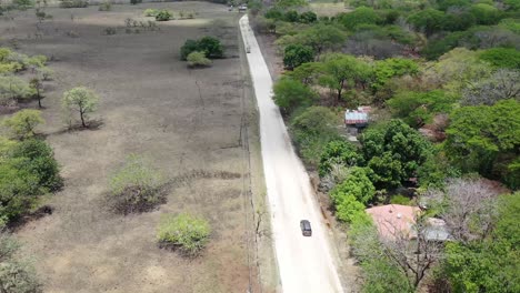 grey vehicle turning right on dirt road junction in costa rica with truck passing left, aerial dolly follow behind shot