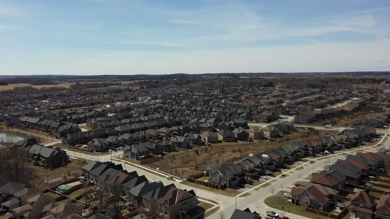 Elevated perspective of a quiet residential community with houses and streets covered in snow, bordering a vast frozen lake on a cold, bright day, illustrating a peaceful winter landscape