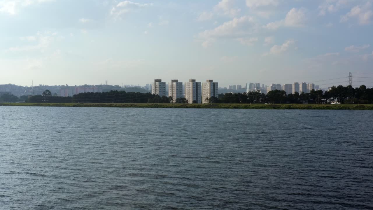 인공 과라피랑가 저수지에서 잔잔한 바다, 야생 동물, 고층 빌딩이 있는 소코로 지역을 향해 브라질 상파울루 남부의 공중 드론 돌리인 및 상승 샷
