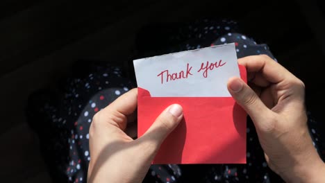 hands holding a thank you note in a red envelope