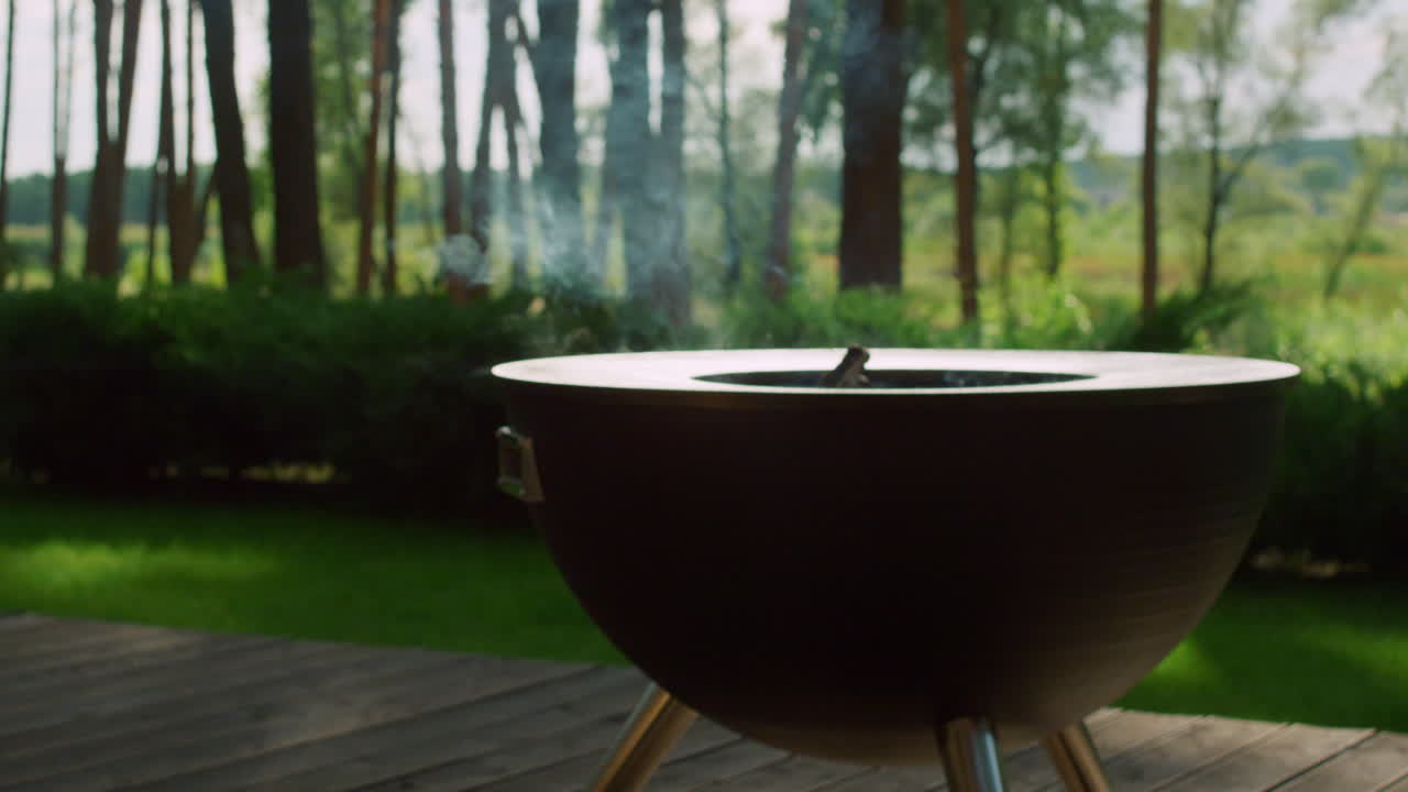 Fumo che sale dalla legna che cova nel barbecue. Griglia vuota nel cortile.