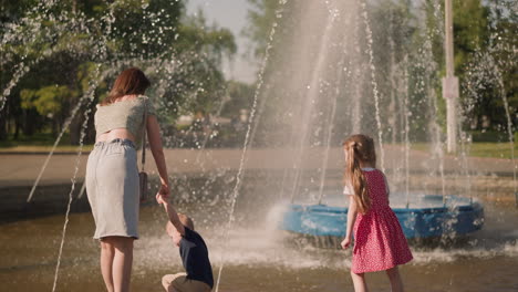 mother and little children enjoy fountain jets in urban park