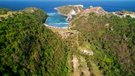 valle de palmeras tropicales con algunas casas indonesias que conducen a la playa de atuh y la isla de batupadasan en nusa penida, bali, indonesia - vista aérea