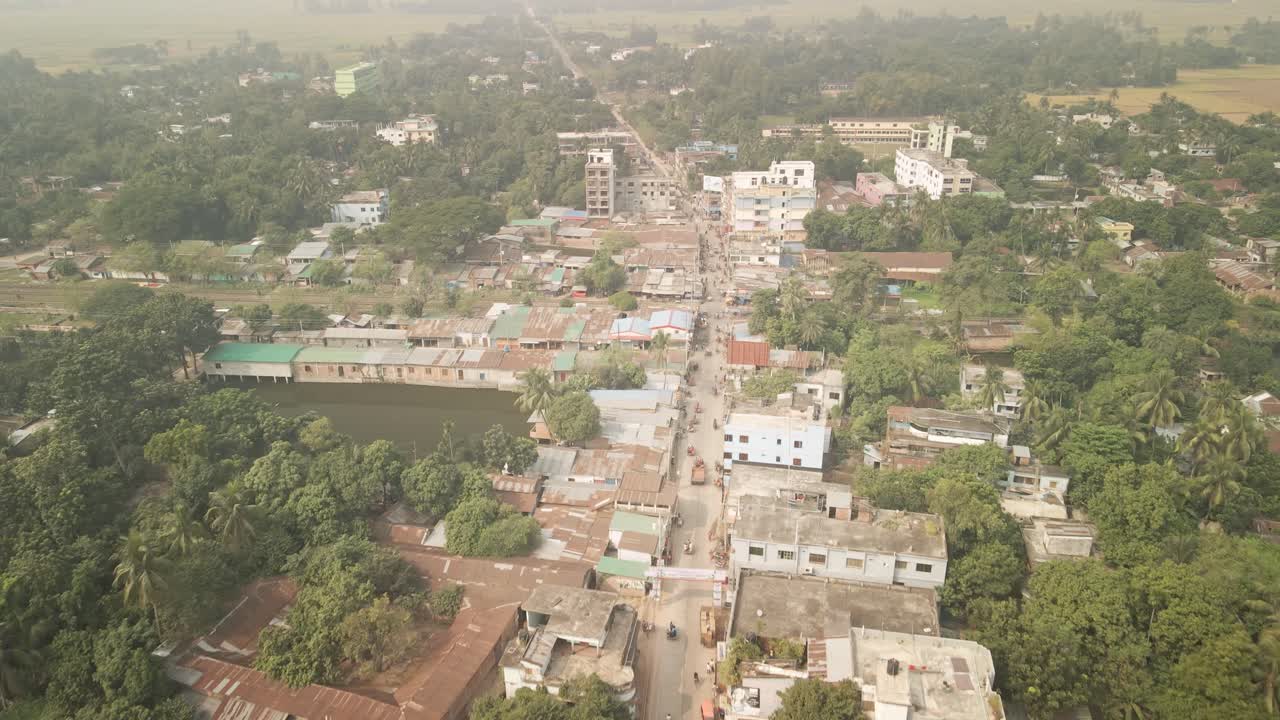 Forward-moving top-down drone shot showing a Bangladeshi town road with local transports, trees, and buildings.