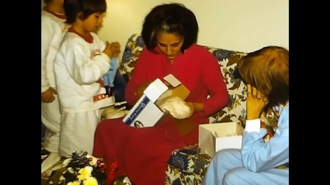 Woman and Child Opening Gifts on Couch. CIRCA USA - 1970s: A woman and child in a 1970s video archive from the USA excitedly open gifts together on a couch.