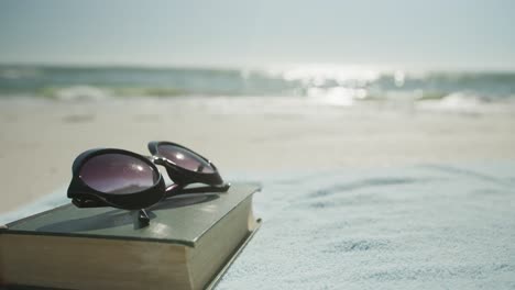 primer plano del libro, gafas de sol y toalla en la playa, en cámara lenta, con espacio para copiar