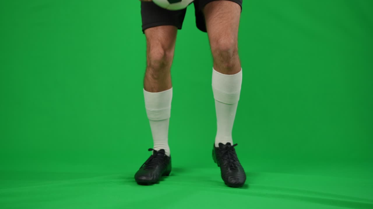 Unrecognizable man juggling football ball on green screen. Legs of young confident Caucasian sportsman training at chromakey background mockup. Skill and sport concept.