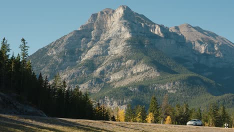 Los-Automóviles-Viajan-Por-Una-Carretera-Frente-A-Un-Gran-Acantilado-Contra-Un-Cielo-Azul-Y-Un-Bosque-Cerca-De-Las-Montañas-Rocosas-De-Canadá-En-Banff,-Alberta,-Canadá.