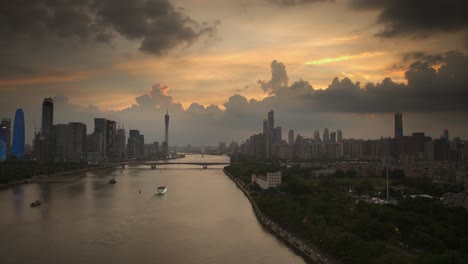 Vista-Aérea-Del-Ferry-Que-Navega-Por-El-Río-Perla-Con-El-Horizonte-De-Guangzhou-Al-Atardecer-En-Guangdong,-China