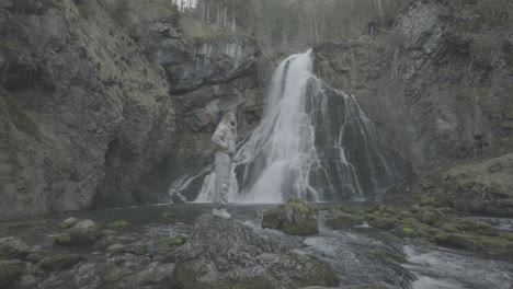 woman standing by a waterfall in a misty forest