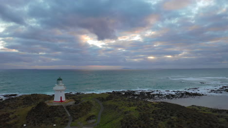 Aerial-view-flying-back-onto-shore-as-Waipapa-Lighthouse-stands-proud-along-the-New-Zealand-coastline