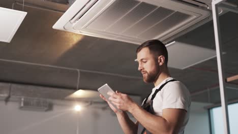 Porträt-Eines-Erwachsenen-Mannes-In-Arbeitsuniform-Mit-Einem-Tablet,-Der-In-Einem-Modernen-Büro-Eine-Industrielle-Klimaanlage-Installiert-Und-Software-Konfiguriert