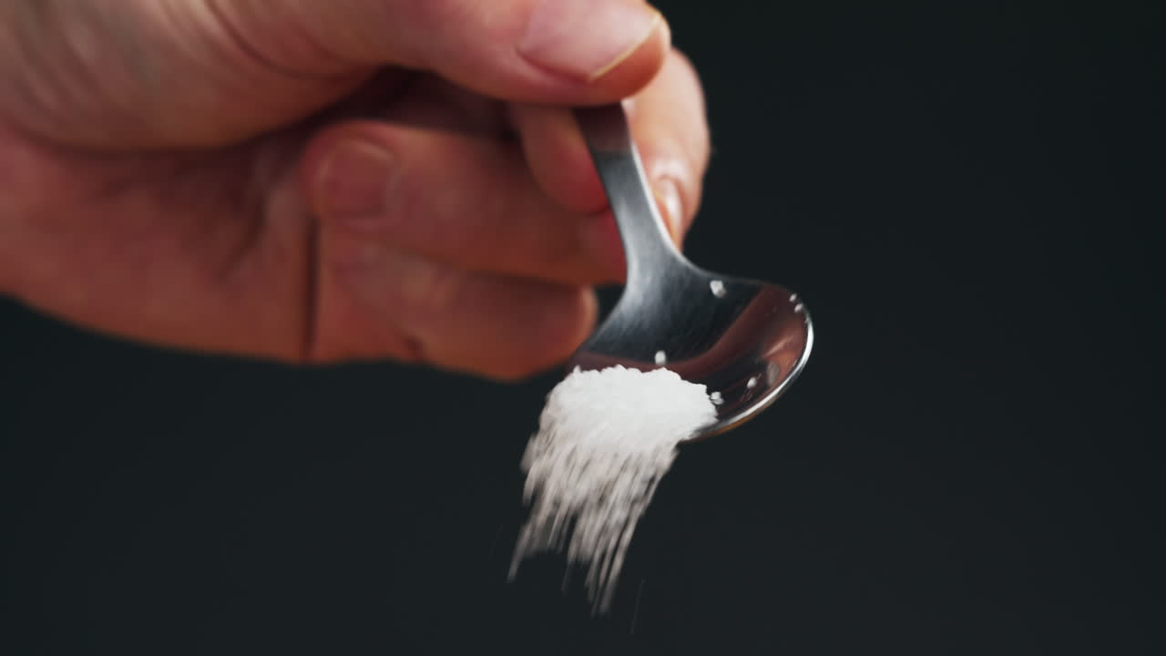 White salt on spoon close-up macro. Spice for food. Sea salt for bath. Man hand srewing salt on table. High quality 4k footage
