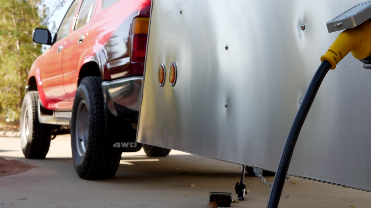 캠프장에서 전기 연결 플러그가 있는 금속 눈물방울 여행 트레일러와 suv 견인 차량 타이어의 측면을 따라 왼쪽으로 미끄러집니다.