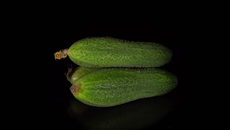 green-skinned cucumbers revolve on a black background.