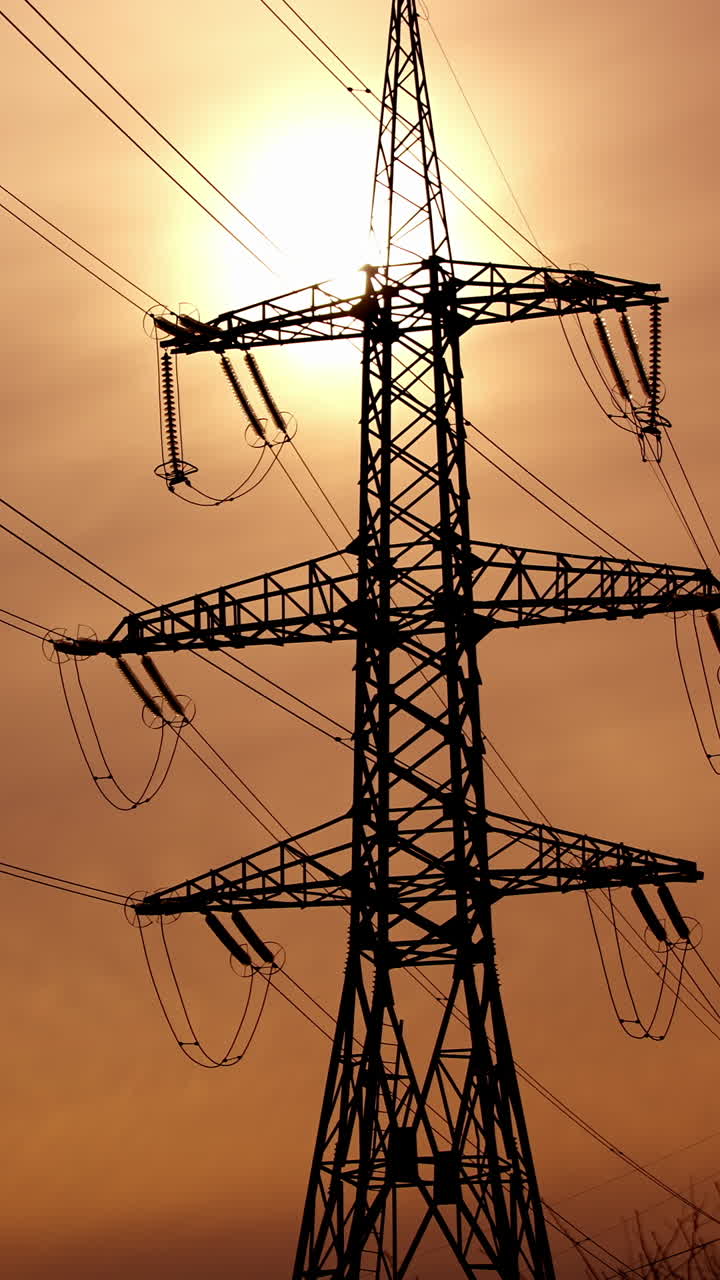 Transmission lines against the evening sky. High-voltage electric towers with wires on the setting sun background. Black pylons with electricity. Vertical video