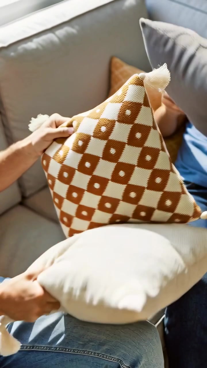 Video vertical: Hombre extendiendo la mano izquierda, levantando almohadas hacia una mujer en el sofá, en jeans para una guerra de almohadas.