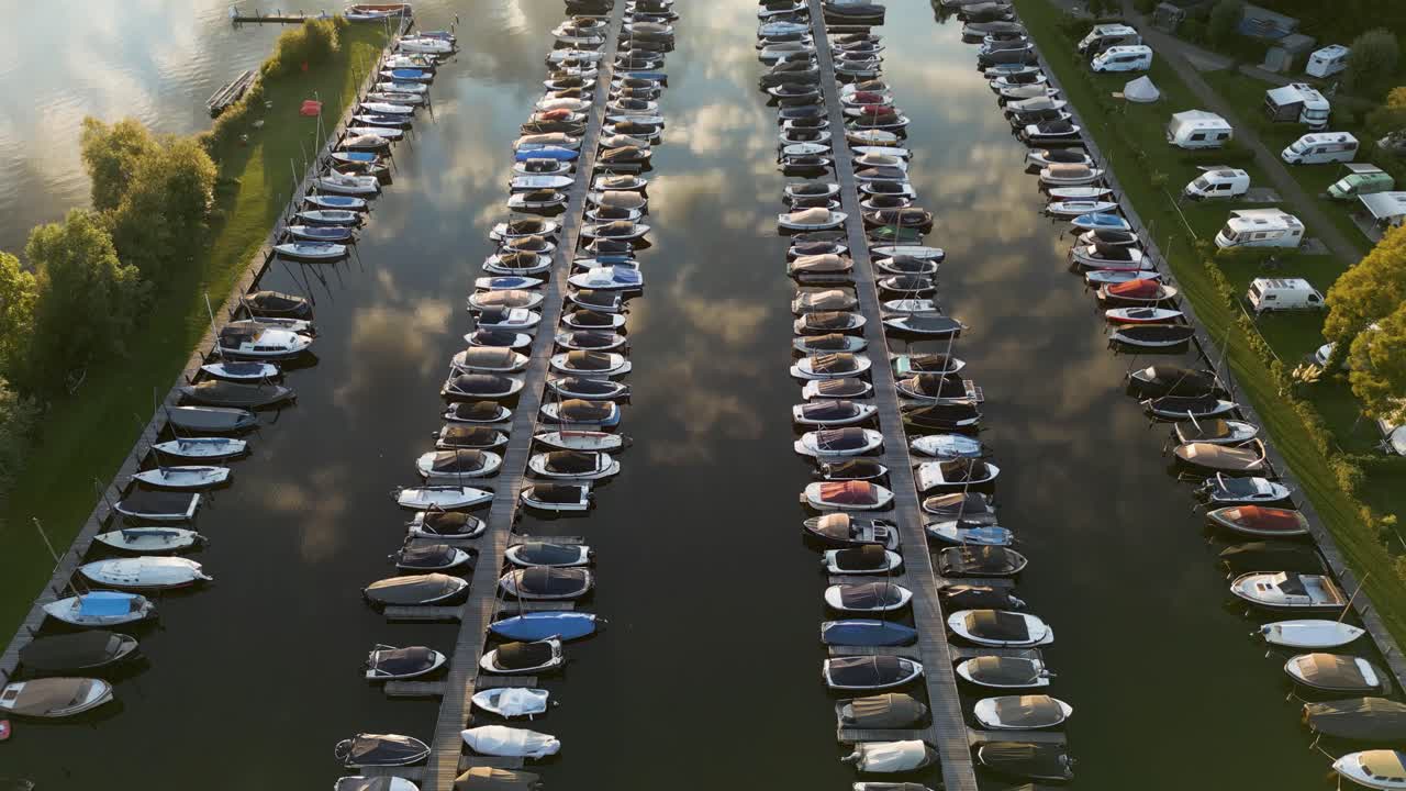 Drone footage of a marina full of moored boats with reflections in the water at sunset
