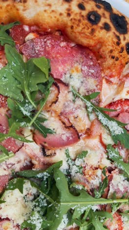 close-up of a gourmet pizza with bacon, ham, and arugula