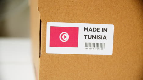 hands applying made in tunisia flag label on a shipping cardboard box with products