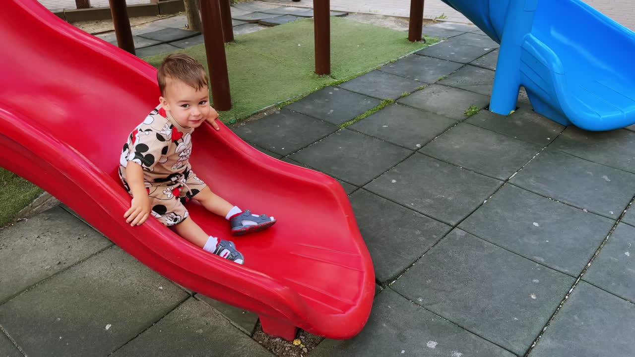 Dark-haired toddler boy goes down by the slide. Joyful energetic child runs the stairs.