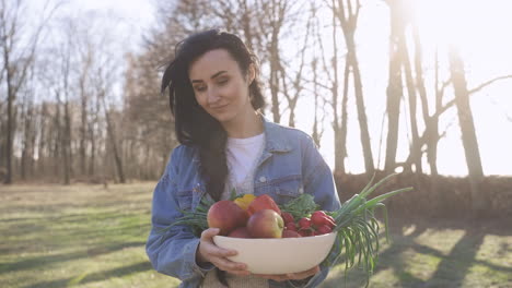 caucasian woman holding a tray with fruits and vegetables while walking through the countryside