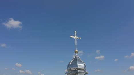 a silver cross on top of a church spire against a blue sky