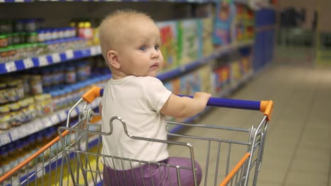 Little-baby-sitting-in-a-grocery-cart-in-a-supermarket,-waiting-for-her-mother-to-come-back-with-purchases.-Family-shopping-with