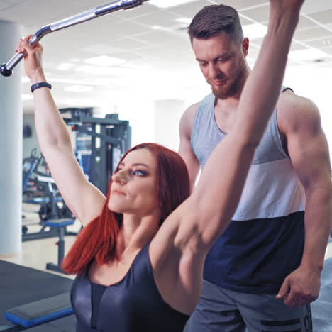 young athletic woman pulling the bar on herself while sitting in the gym. beautiful girl doing workout with her personal trainer. sports and healthy lifestyle.