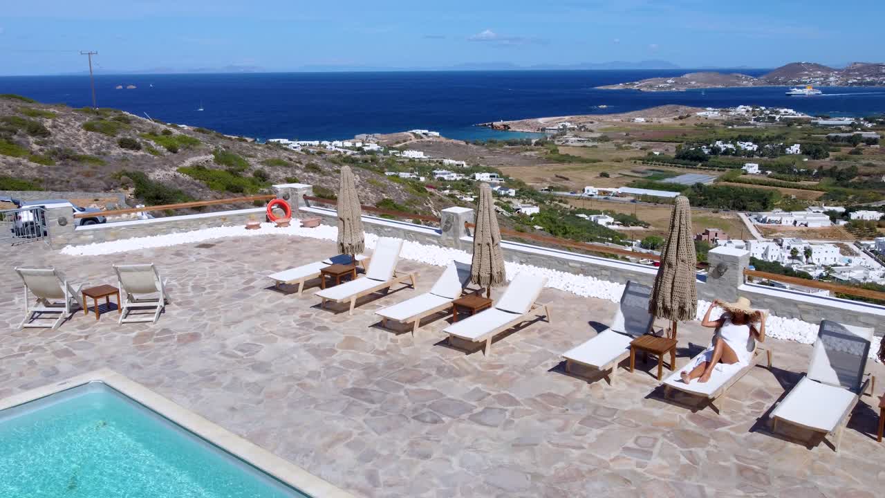 Revealing Aerial Panoramic View over Relaxing Woman in Hotel Pool Terrace to Seaside Paros Landscape