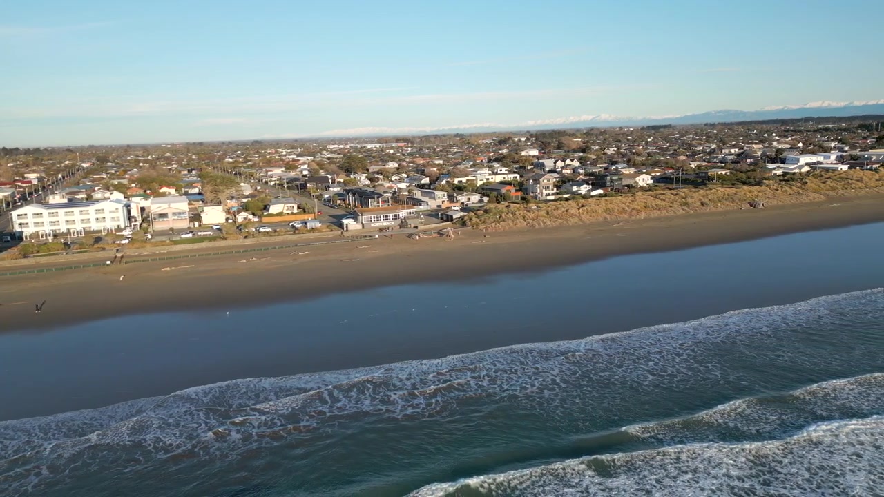 Case sulla spiaggia di New Brighton, dune e onde all'alba, Christchurch, Nuova Zelanda, ripresa con drone in allontanamento, 4K 60FPS