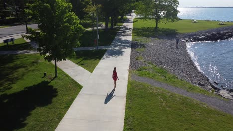 aerial tilt down shot young women walking along a waterfront wearing a cute red dress