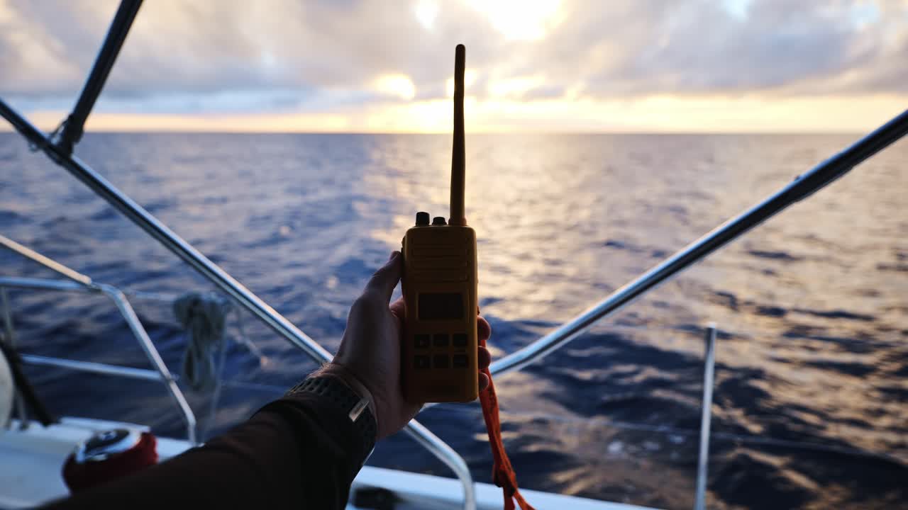 Hand gripping VHF radio on a sailboat with deep blue ocean in the background
