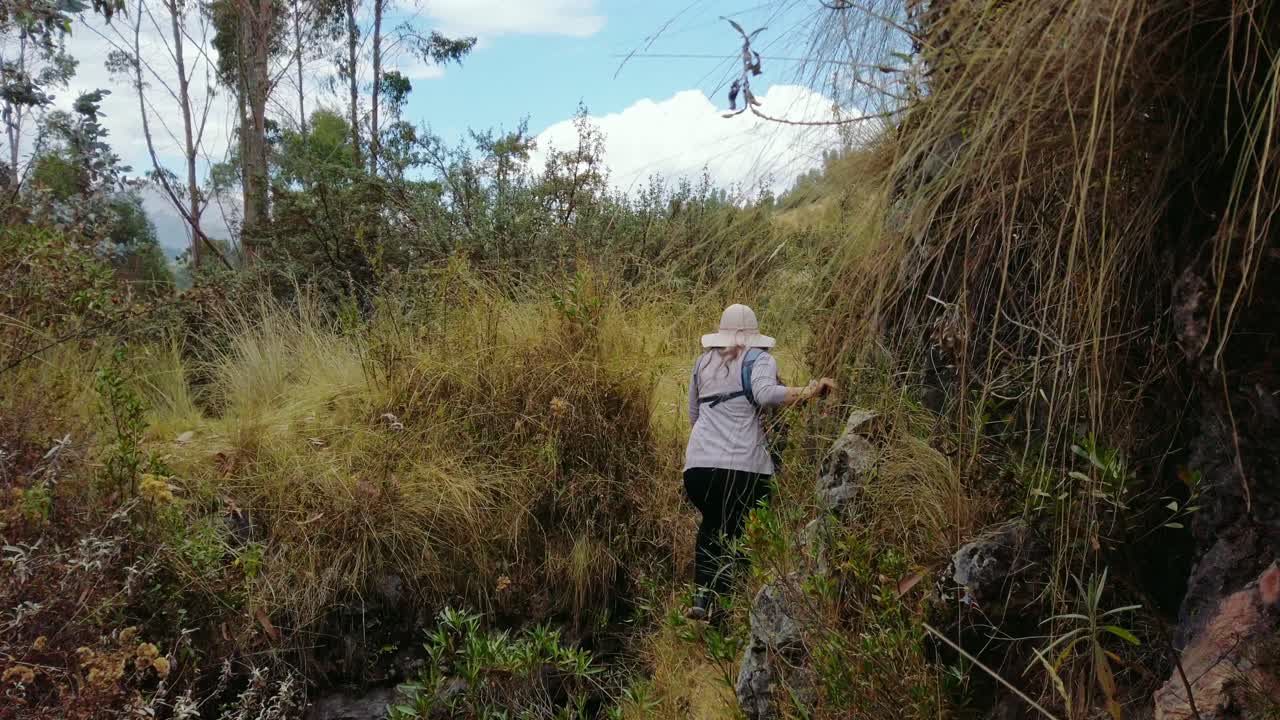 Woman walks along a narrow ancient Inca trail surrounded by nature near Cusco, Peru.