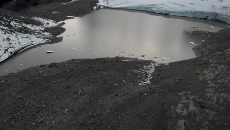 Aerial-view-of-the-glacial-lake-of-Claridenfirn-glacier-in-Uri,-Swizerland-at-dusk-with-a-pan-up-view-to-the-glowing-sky-behind-the-alpine-peaks-from-the-floating-icebergs-in-the-water